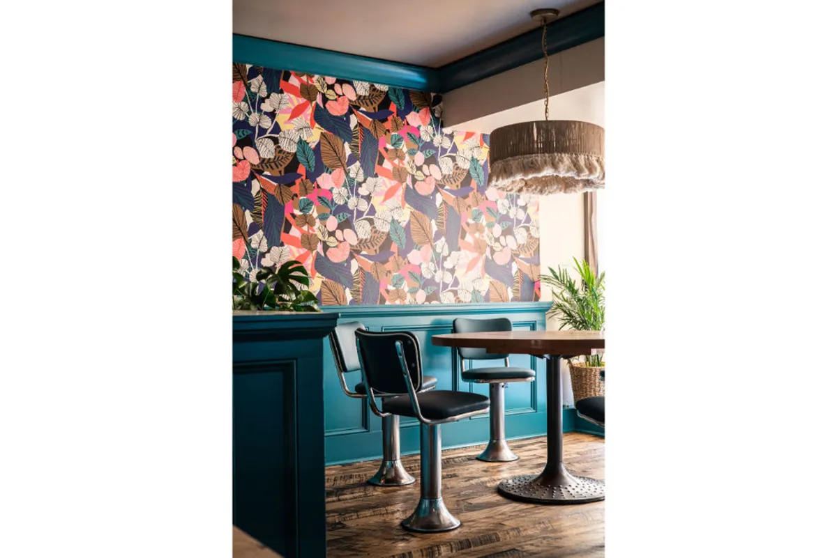 A cheerful dining nook outfitted with colorful floral wallpaper, modern furniture, an indoor plant, and soft lighting. The space is both inviting and vibrant, ideal for casual dining or relaxed moments.